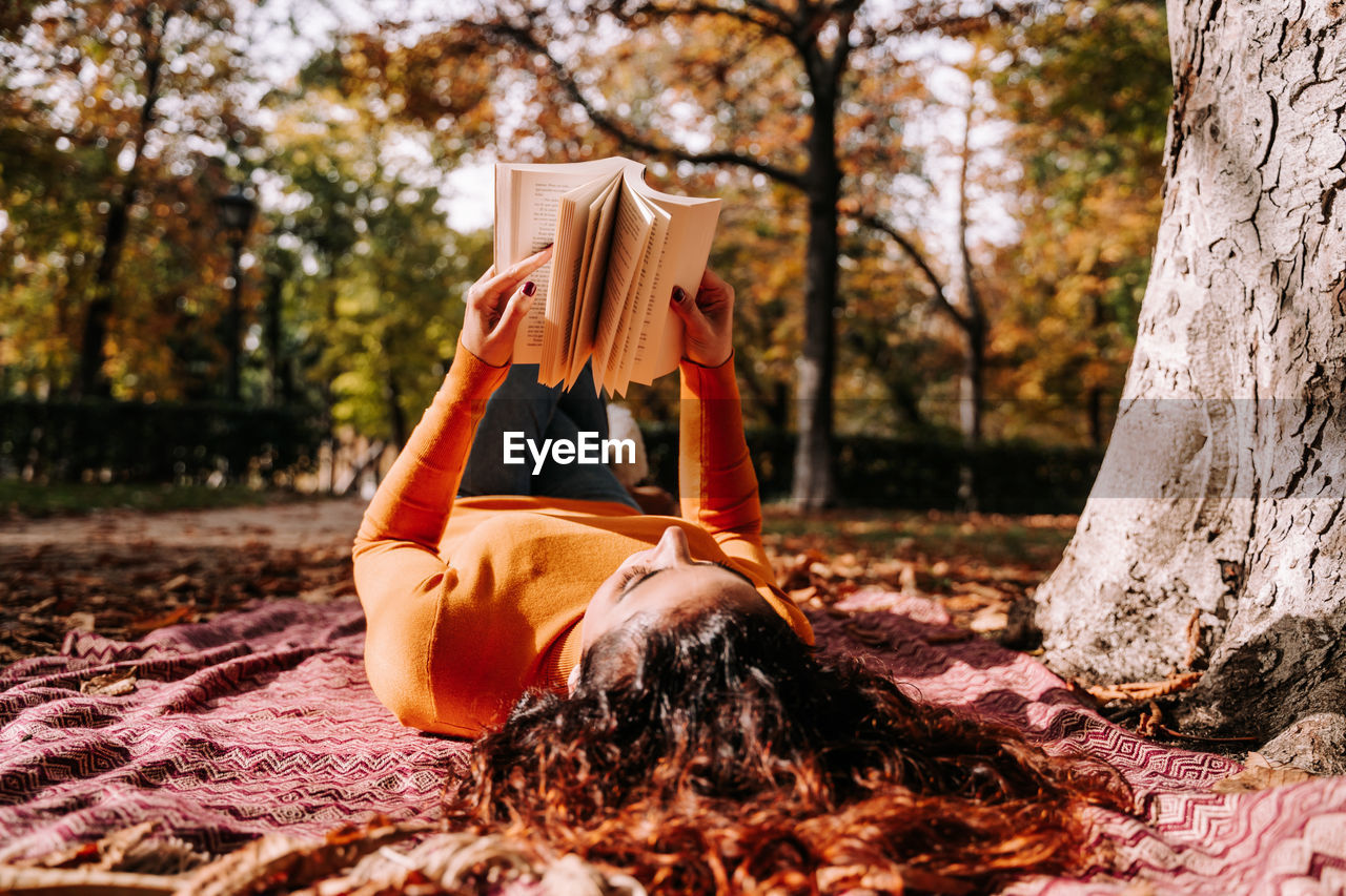 Woman reading book while lying at park during autumn