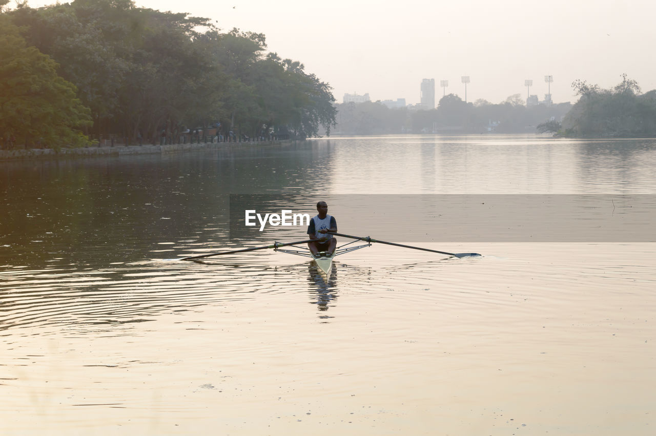 REAR VIEW OF MAN STANDING IN LAKE AGAINST TREES