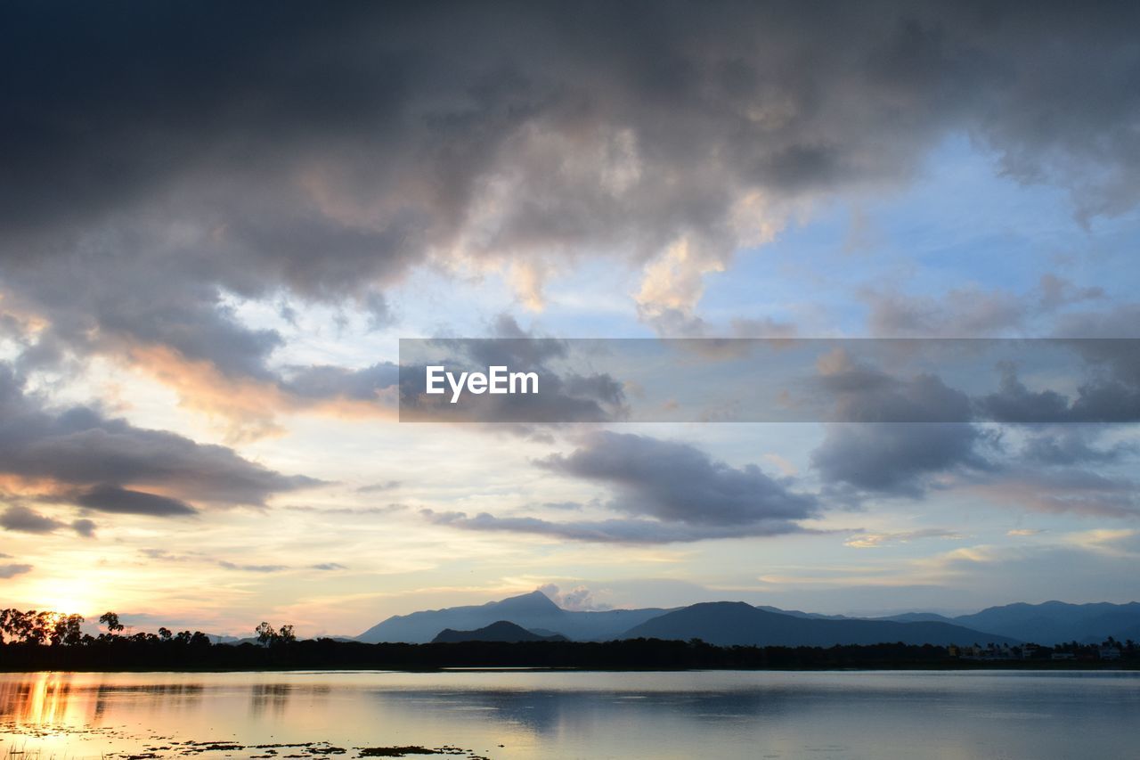 SCENIC VIEW OF LAKE BY SILHOUETTE MOUNTAIN AGAINST DRAMATIC SKY