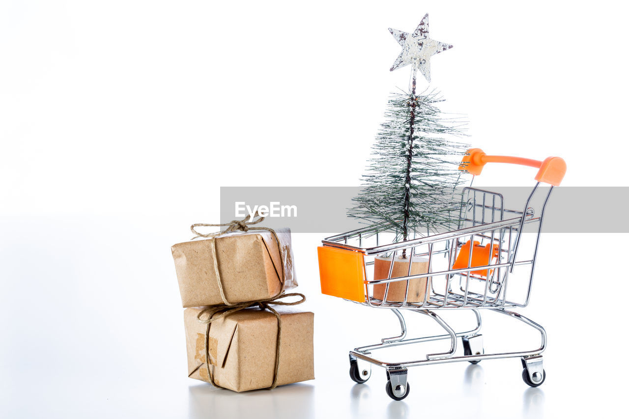 Close-up of christmas tree with gifts and shopping cart against white background