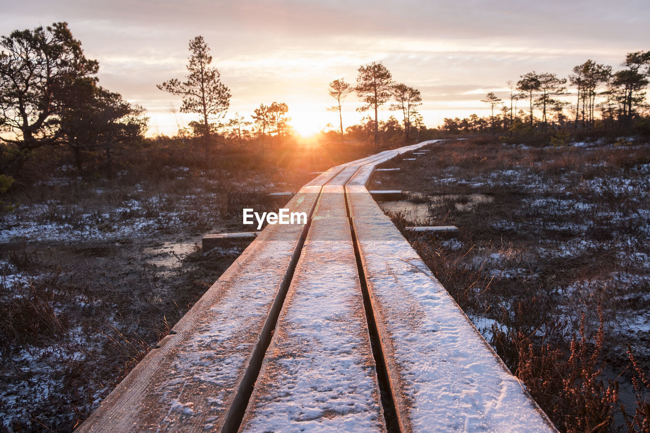 Snow covered footpath against sky during sunset