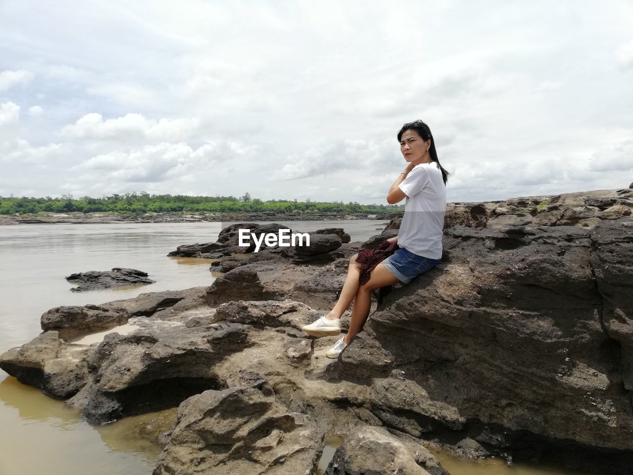 Woman sitting on rock at beach against sky