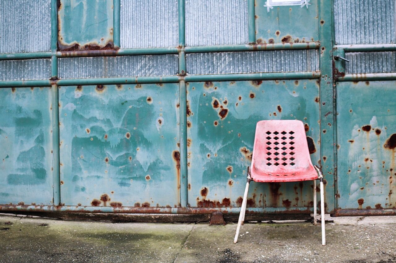 Empty chair against rusty wall