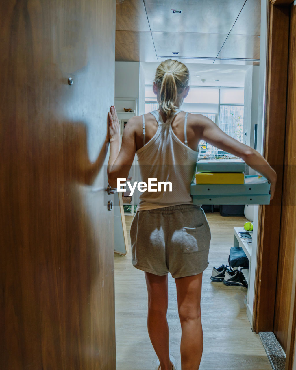 Rear view of woman standing against door at home with pizza boxes