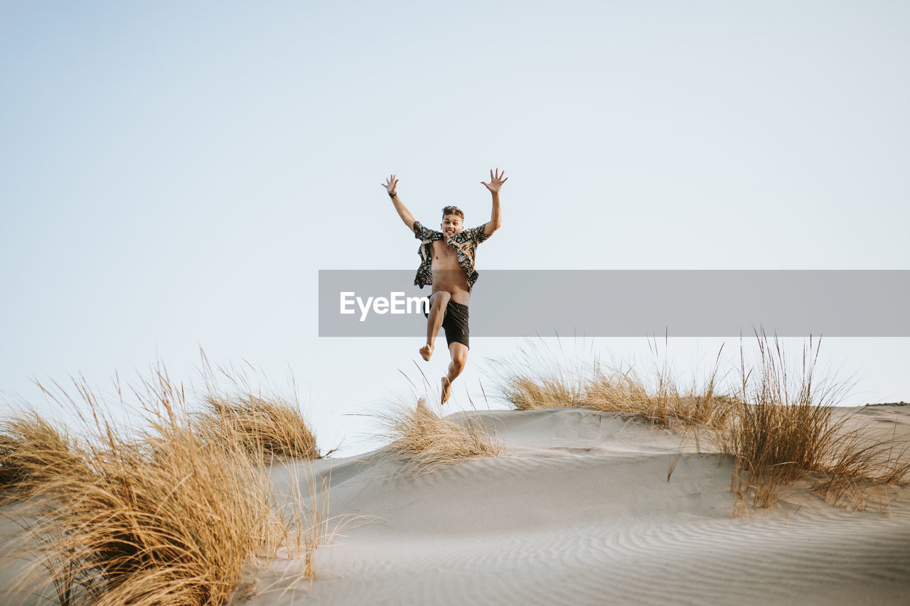 Cheerful young man jumping over sand at almeria, tabernas desert, spain