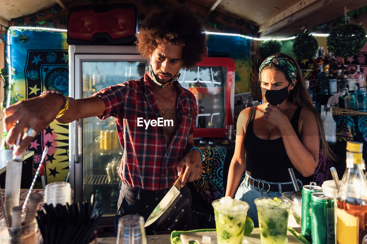 Adult ethnic man and woman standing at counter and preparing drinks for order while working together in outdoor bar