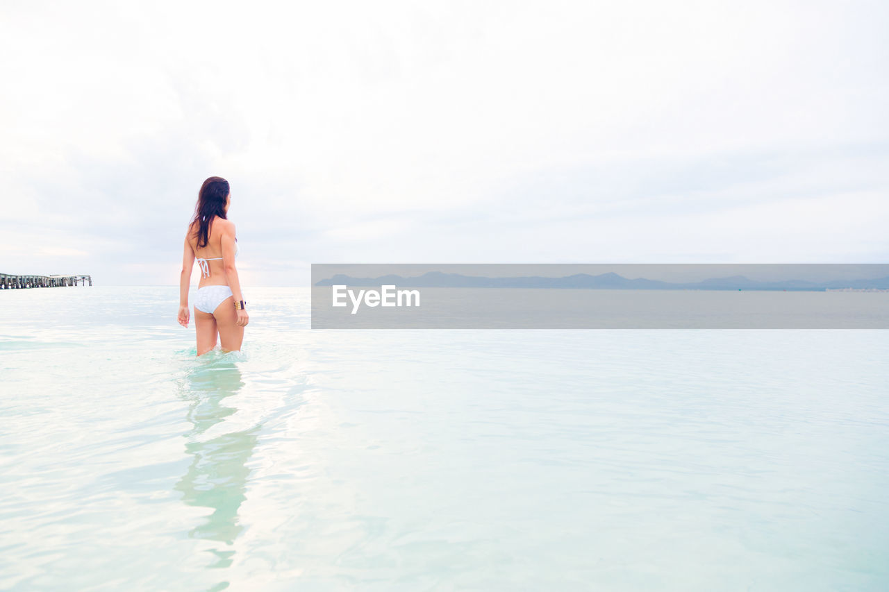 Woman wearing bikini while standing in sea against sky