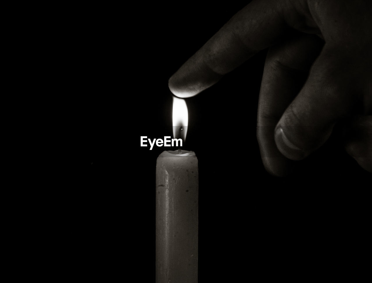 Cropped hand of person touching flame of candle in darkroom