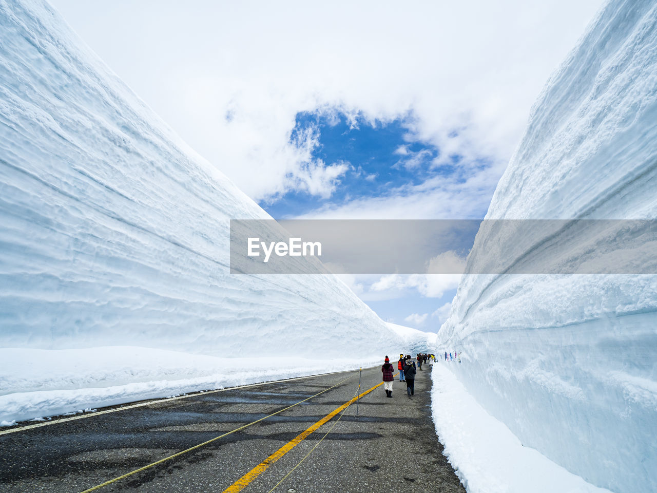 PEOPLE WALKING ON SNOWCAPPED MOUNTAIN ROAD AGAINST SKY