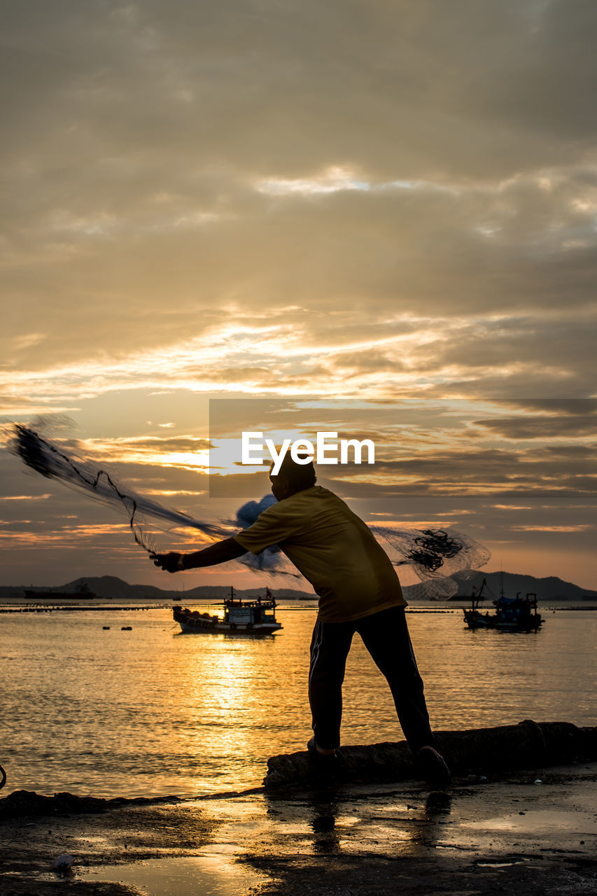 Fisherman throwing net at jetty during sunset