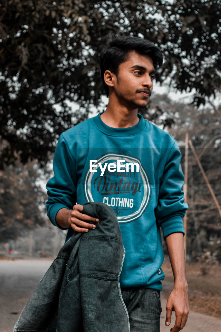 Man holding jacket while standing on footpath