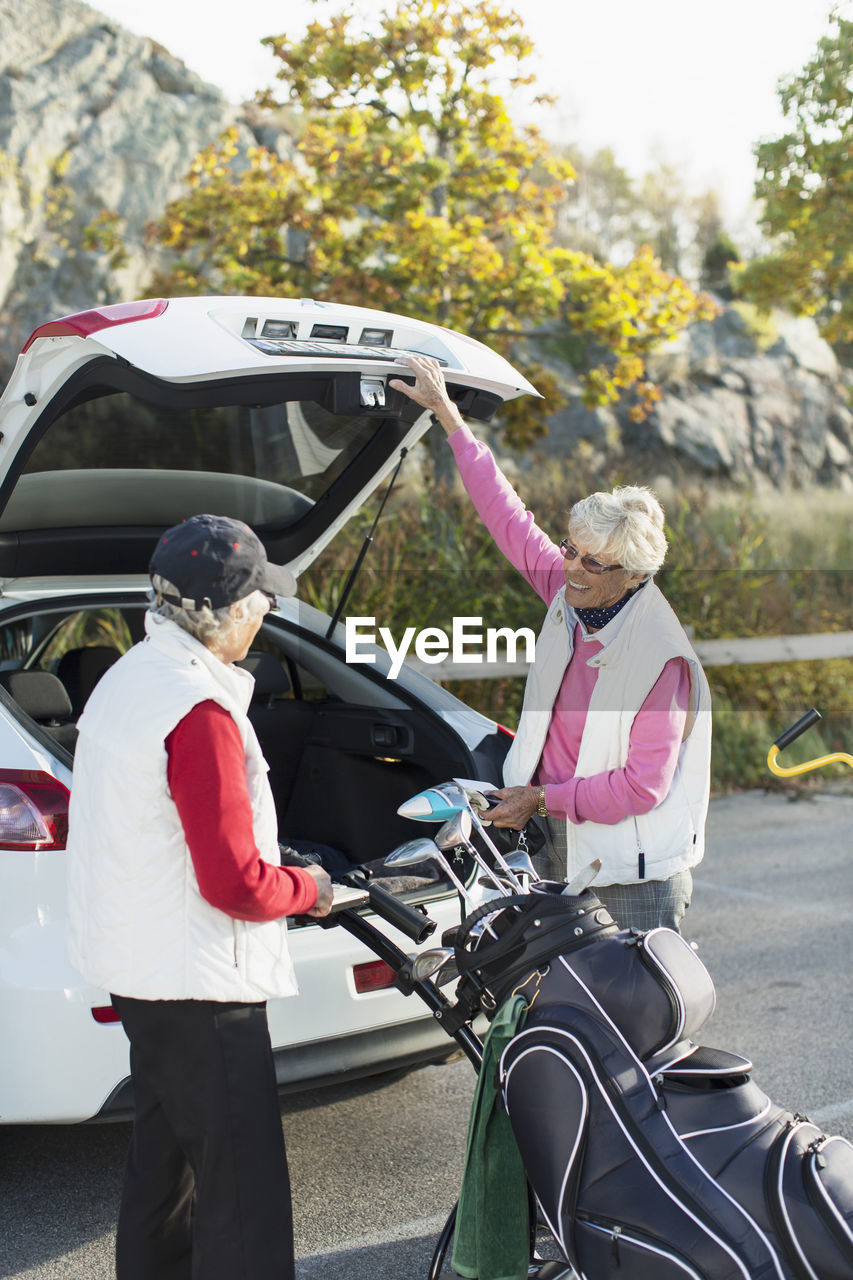 Senior female friends loading golf bag into car boot