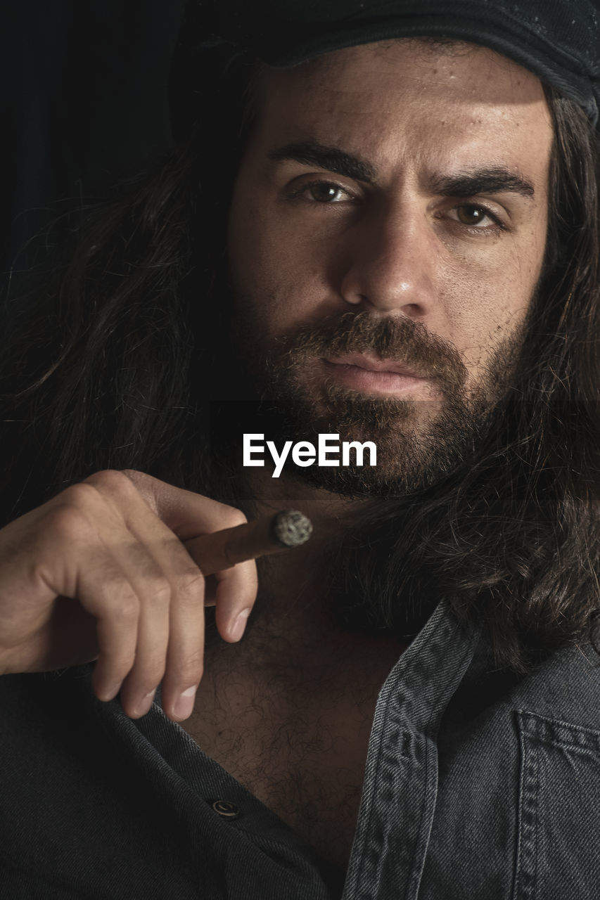 Portrait of man holding cigar on black background