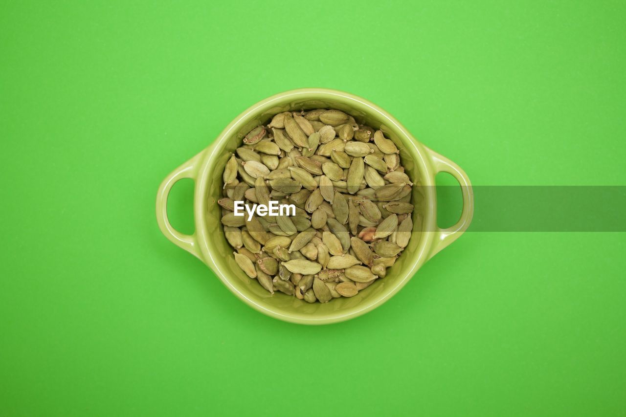 Directly above view of cardamom in bowl on green background