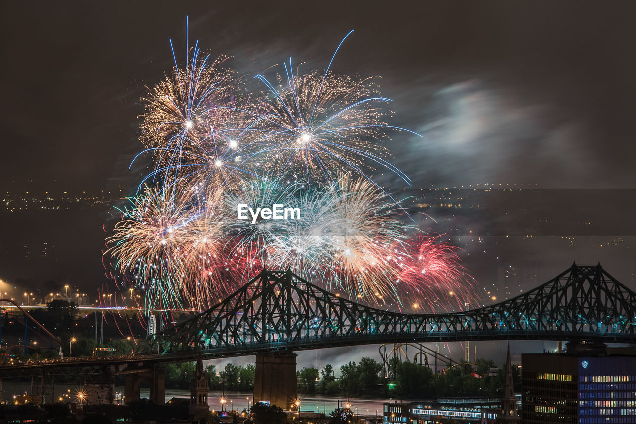 LOW ANGLE VIEW OF FIREWORK DISPLAY OVER RIVER IN CITY