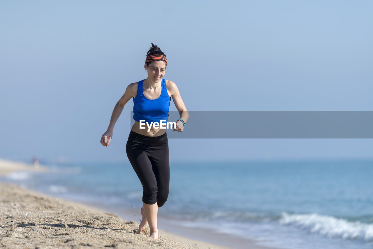 full length of young woman standing on beach against clear sky