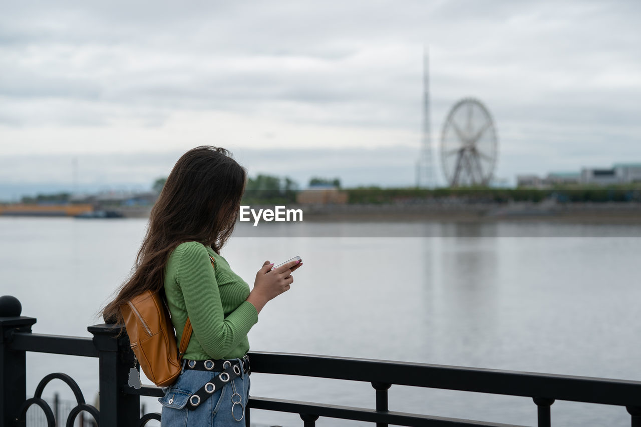 Girl stands on the embankment of the river, looks at the phone. 