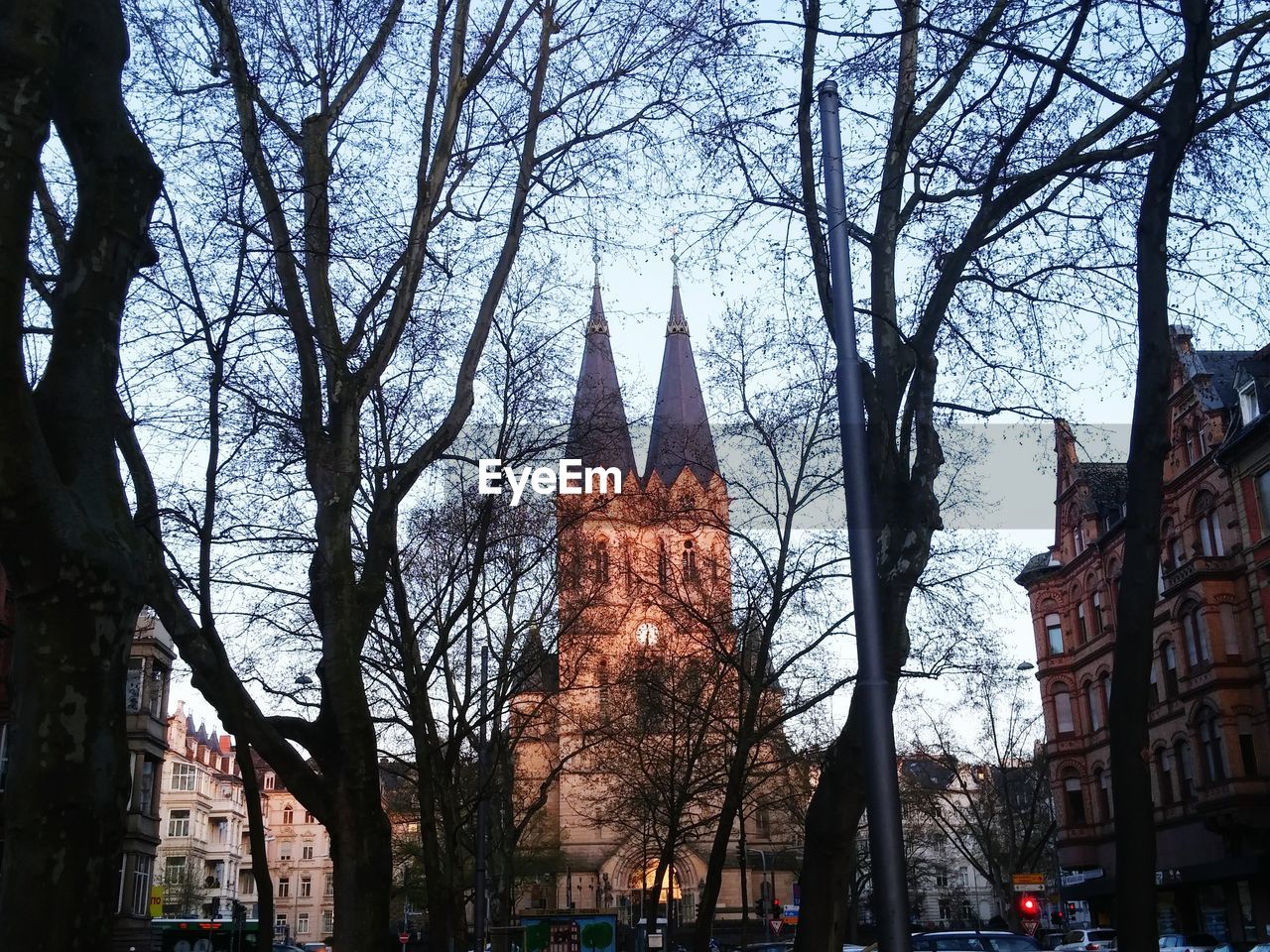 Illuminated building seen through bare trees against sky in city