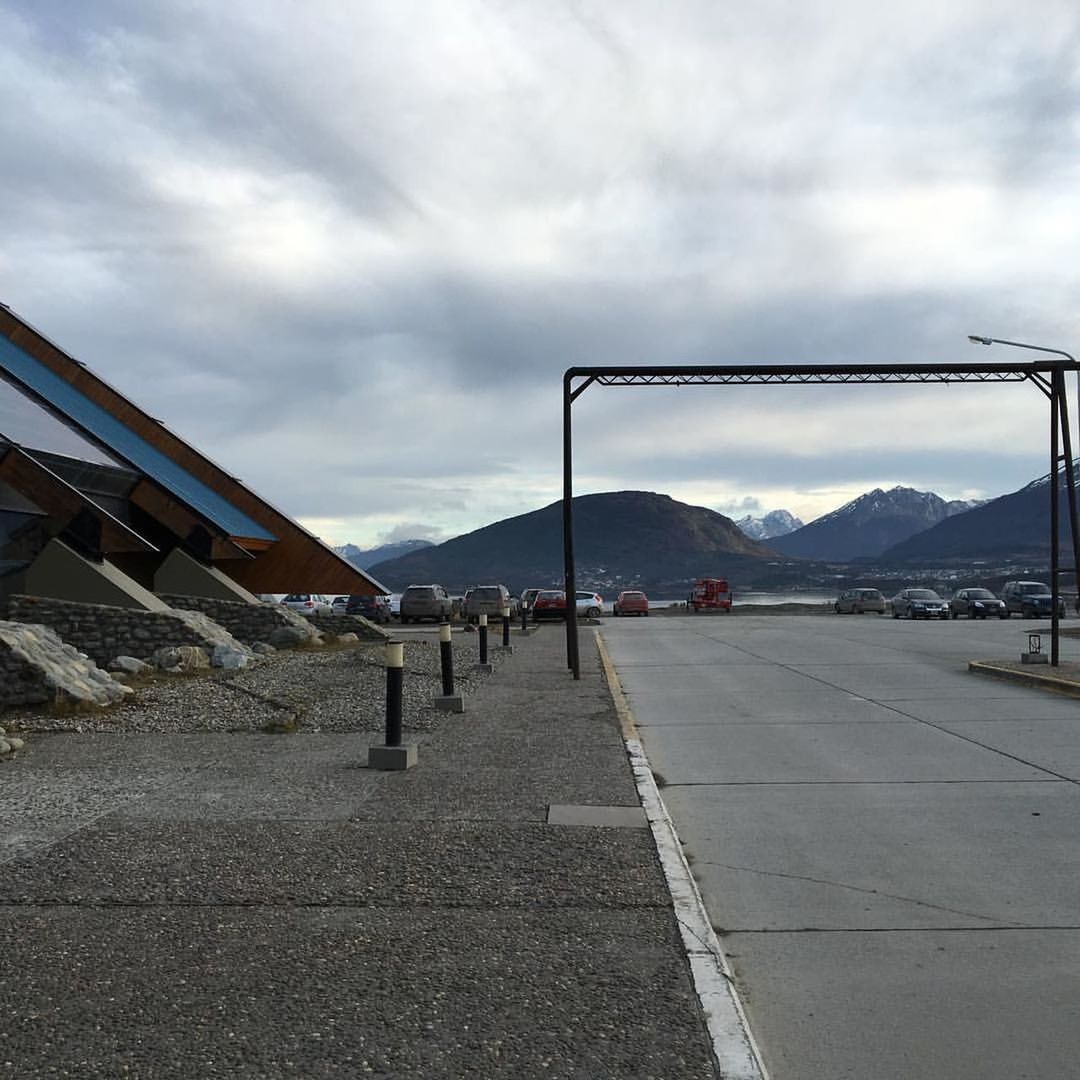 Road leading towards parked cars in front of mountains against cloudy sky