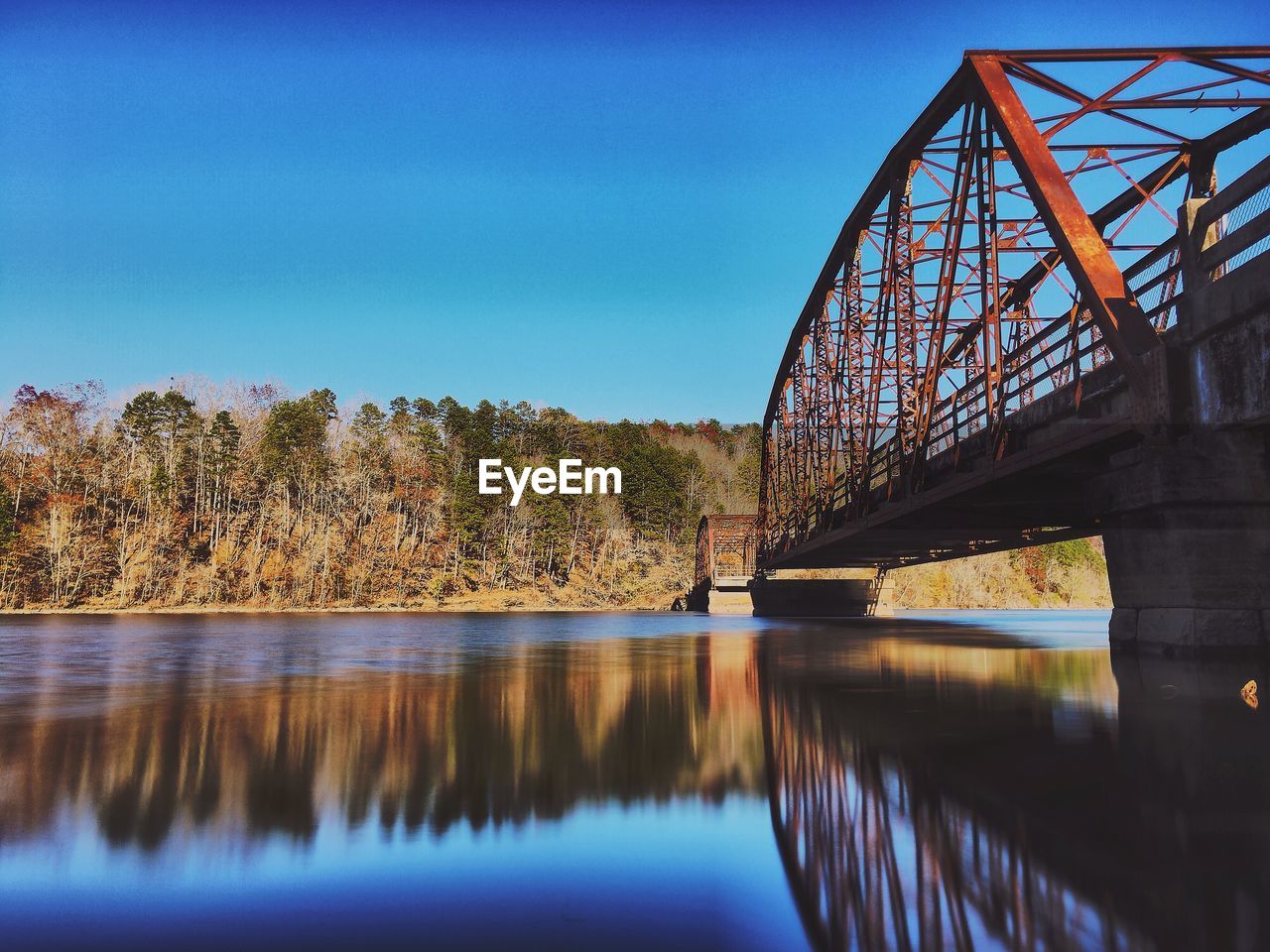 Reflection of bridge on lake against clear blue sky