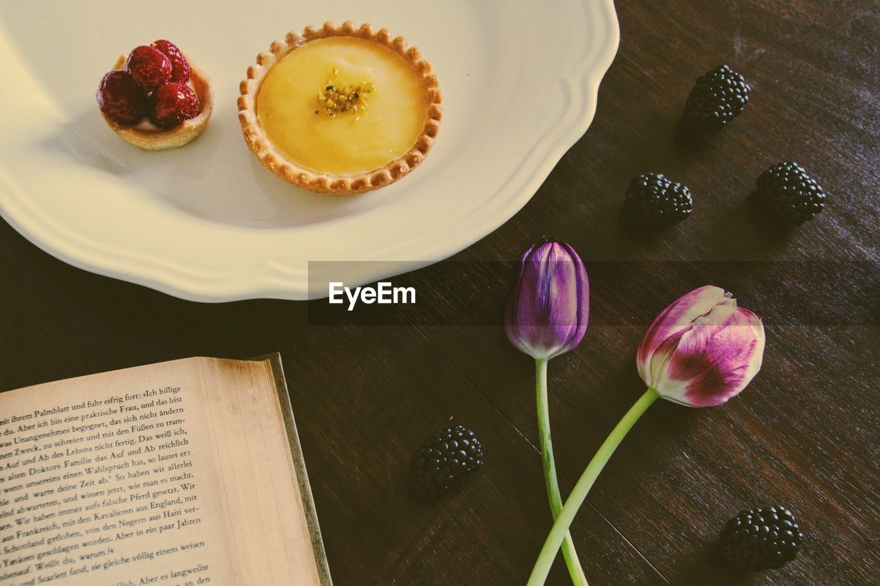 High angle view of lemon tart with purple tulips and book on table