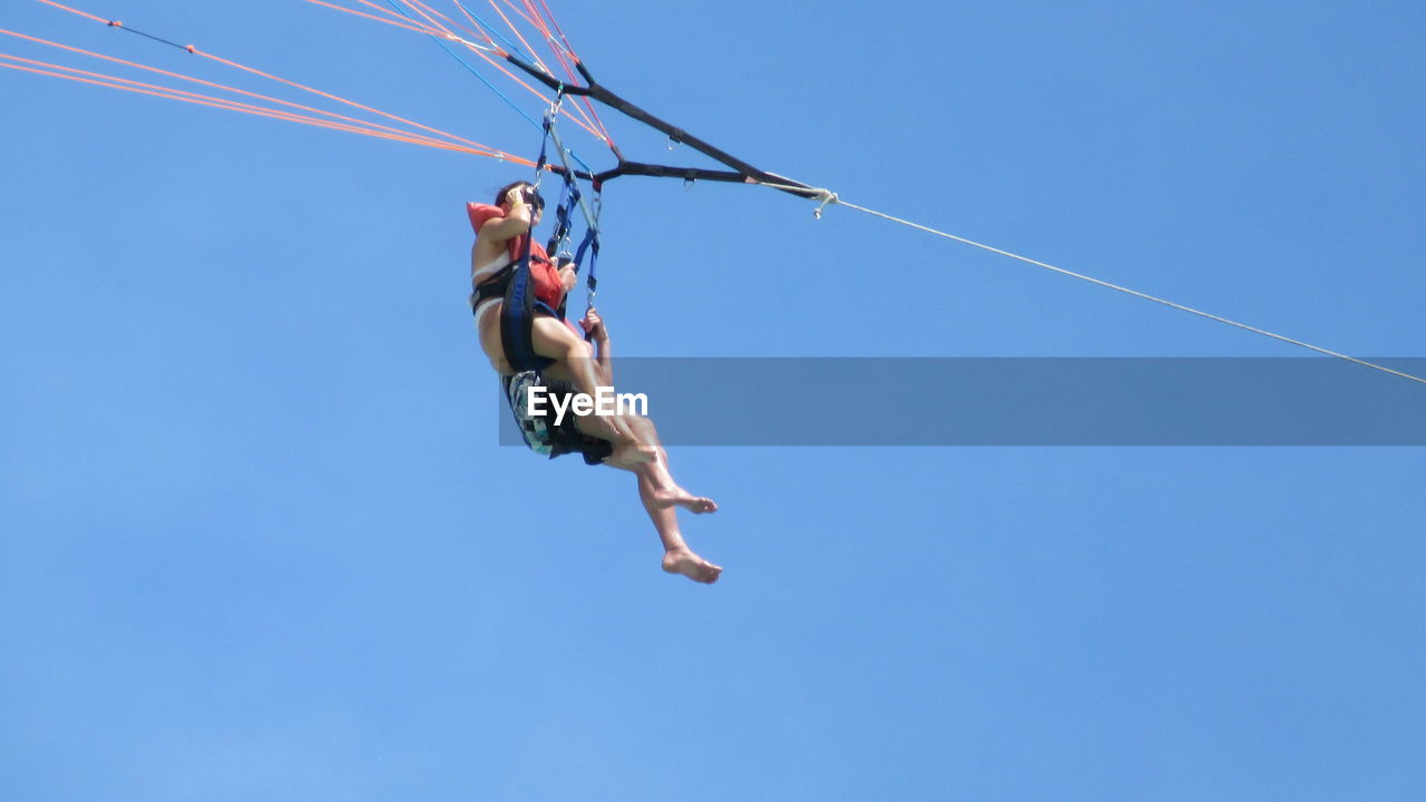 Low angle view of people parasailing against clear blue sky