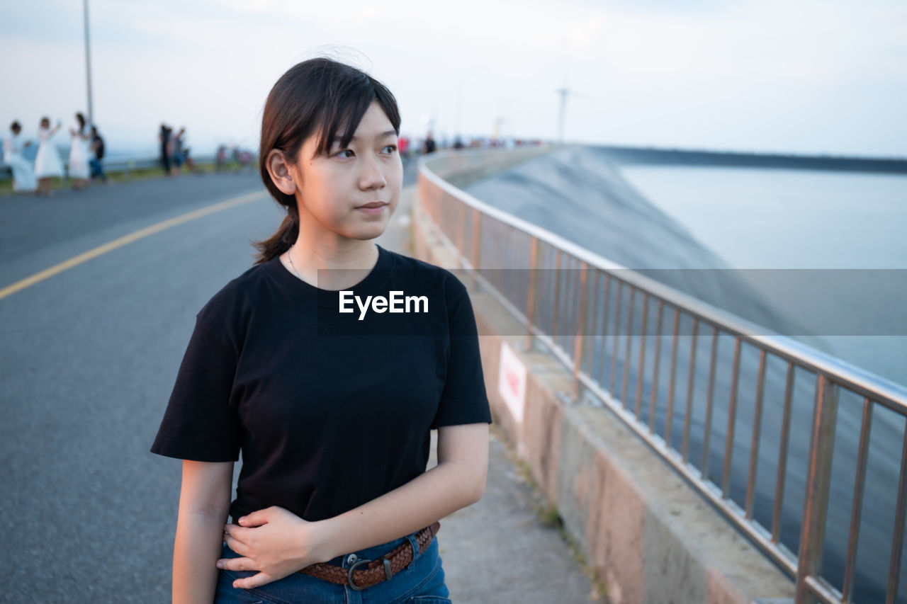 Teenage girl looking away while standing against railing