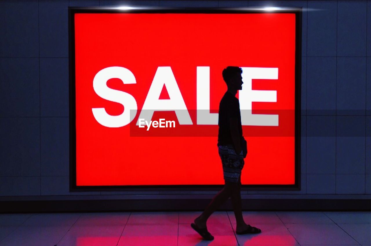 Side view of man walking against sale text in city at night