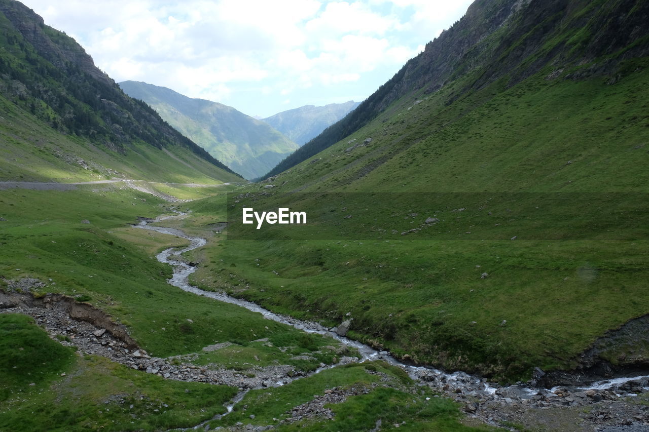 Scenic view of stream amidst green landscape against sky