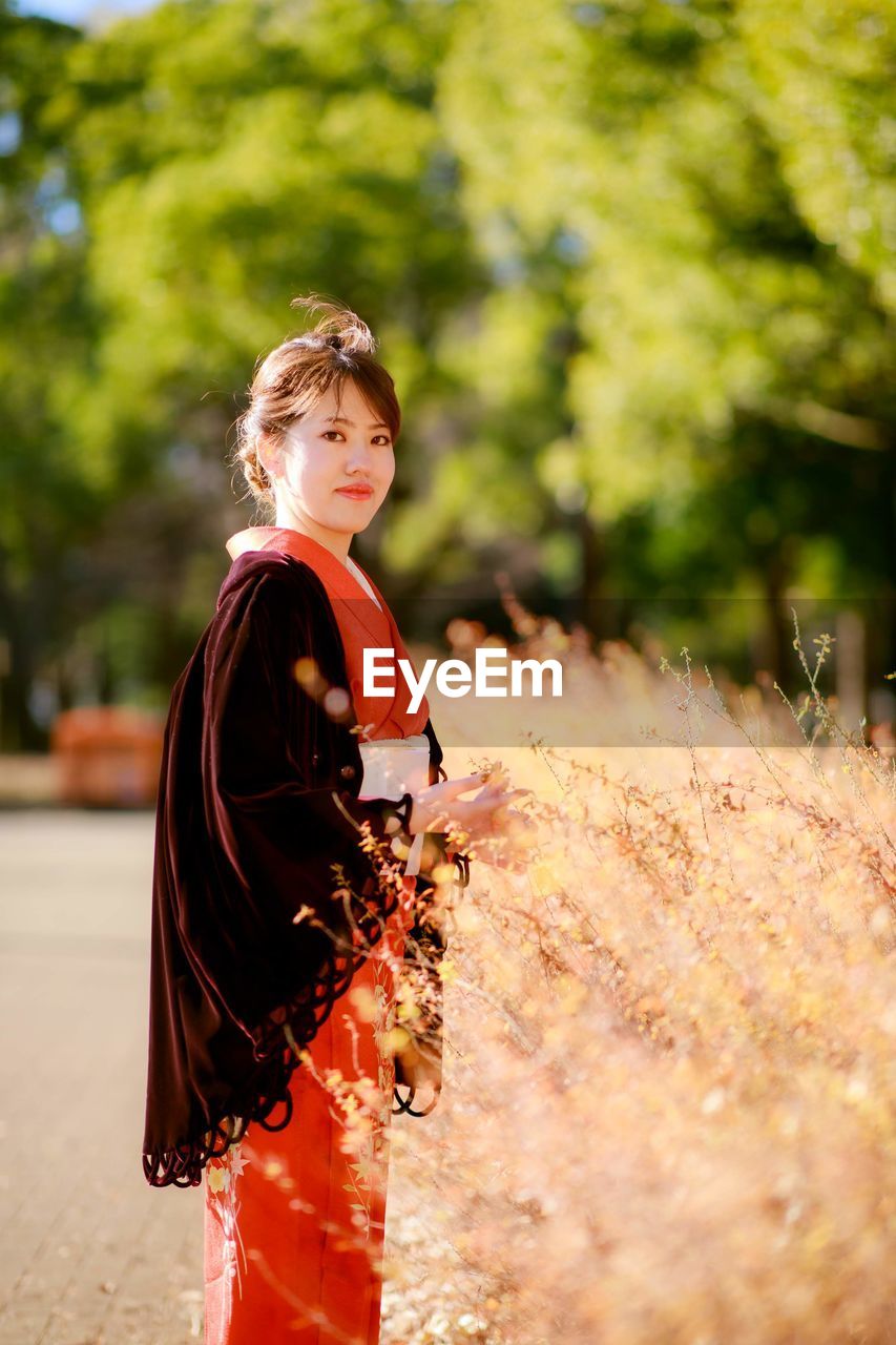 SIDE VIEW OF WOMAN STANDING ON FIELD AGAINST TREES