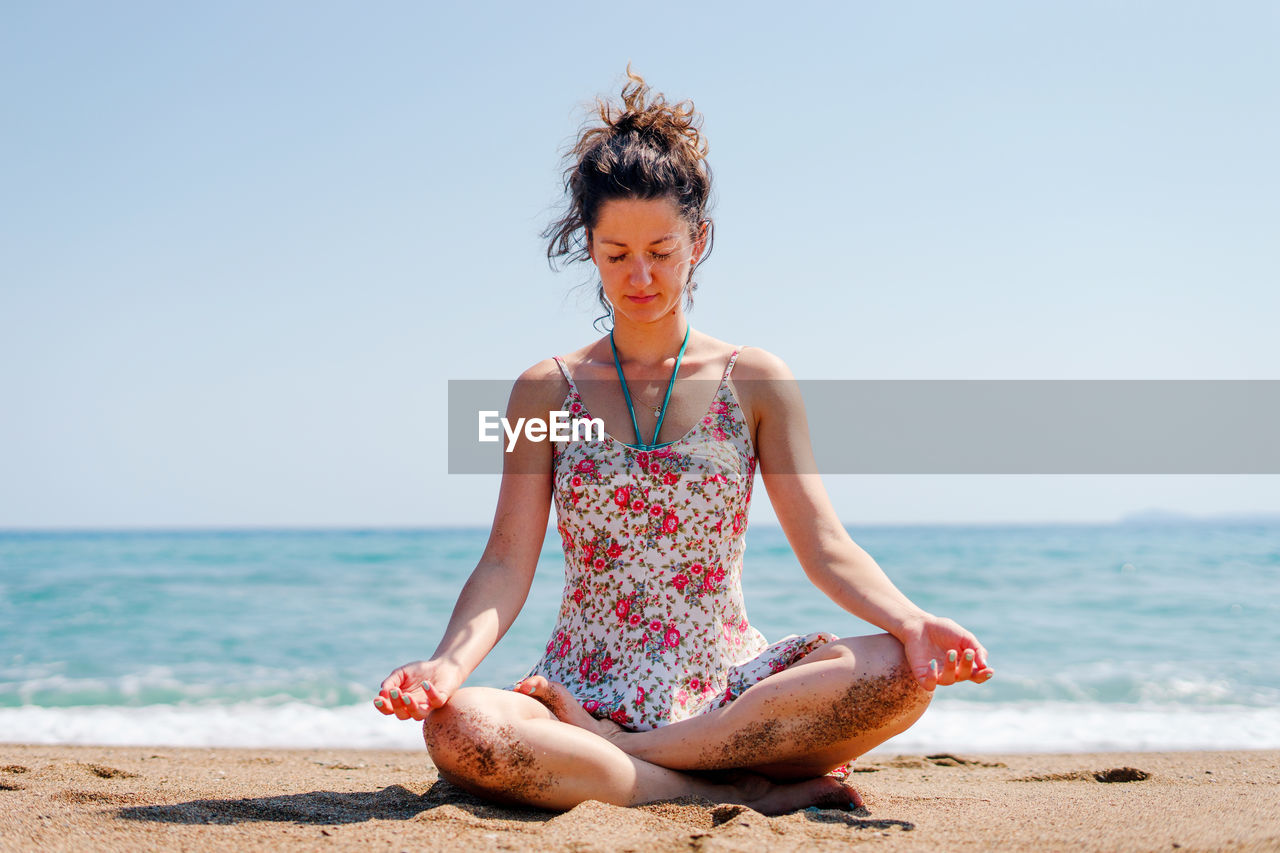 Full length of woman meditating while sitting at beach