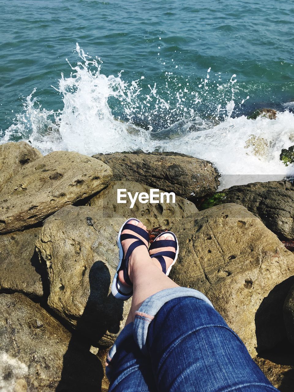 Low section of woman on rock at sea shore