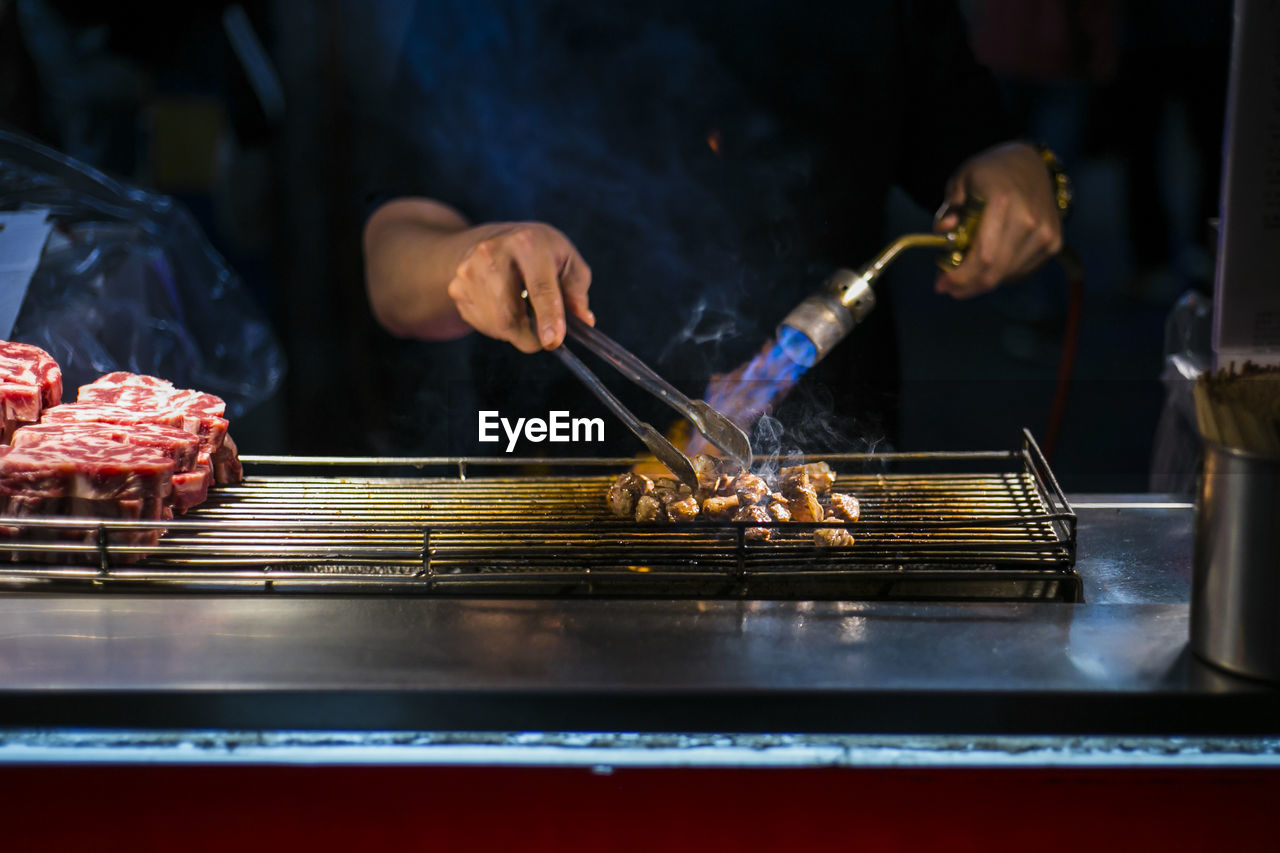 Midsection of chef grilling meat in kitchen