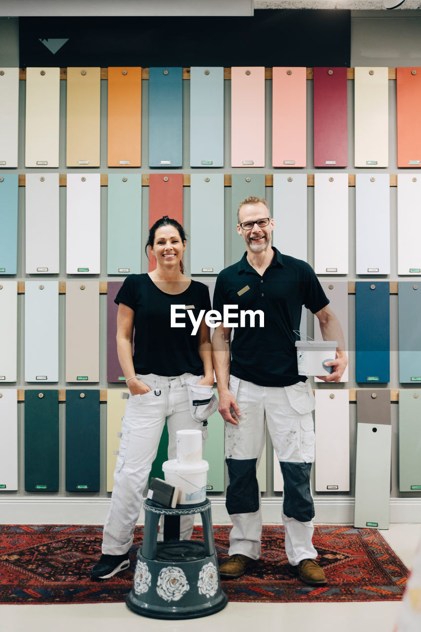 Full length portrait of smiling coworkers standing against multi colored wall in store