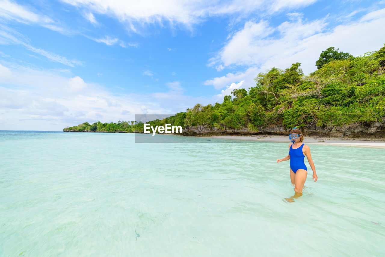 Woman wearing snorkel walking in sea against sky