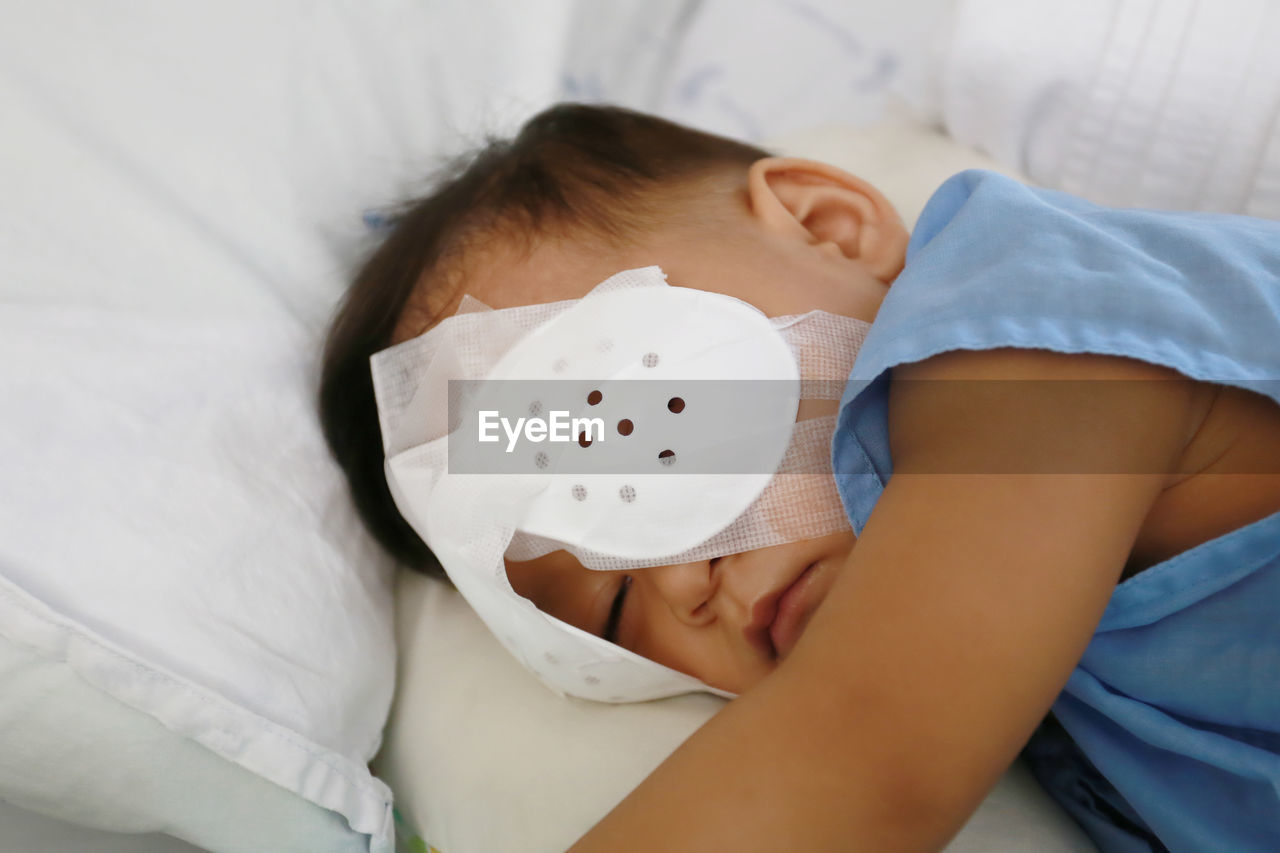 Cute boy with bandage on eye resting on bed