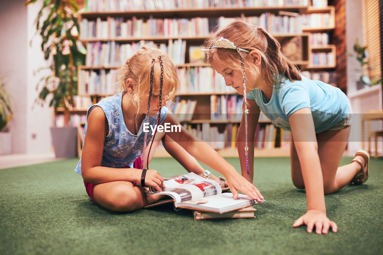 Two schoolgirls reading books in school library. primary school students learning from books
