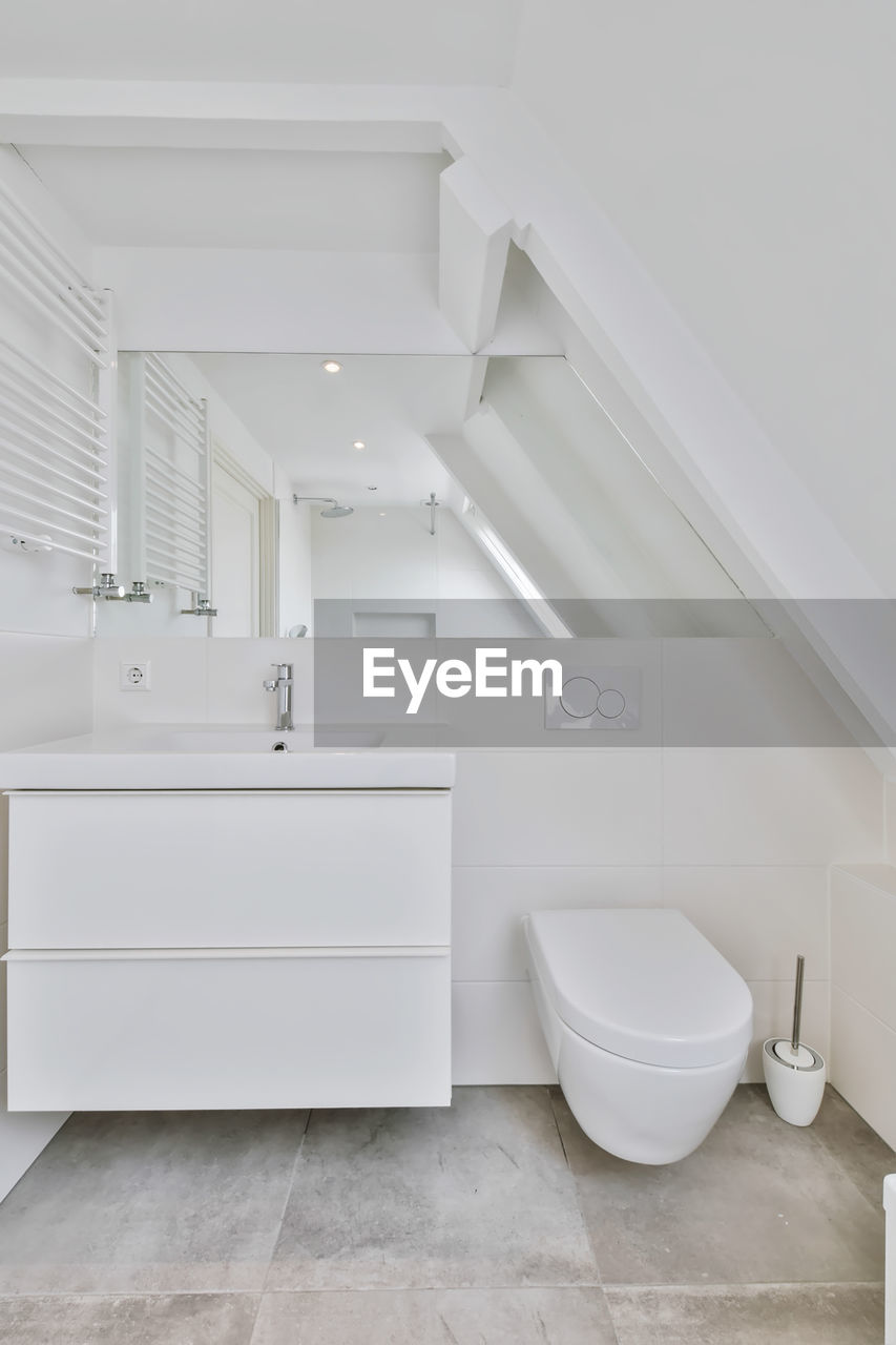 Bathroom with mirrored sink and toilet in the bright attic of the house