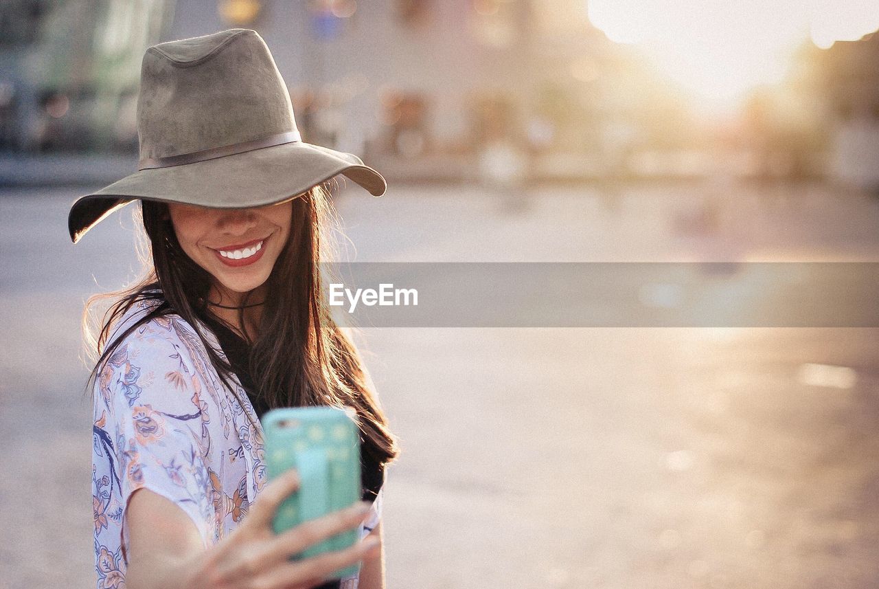 Happy woman taking selfie from mobile phone on street in city during sunset