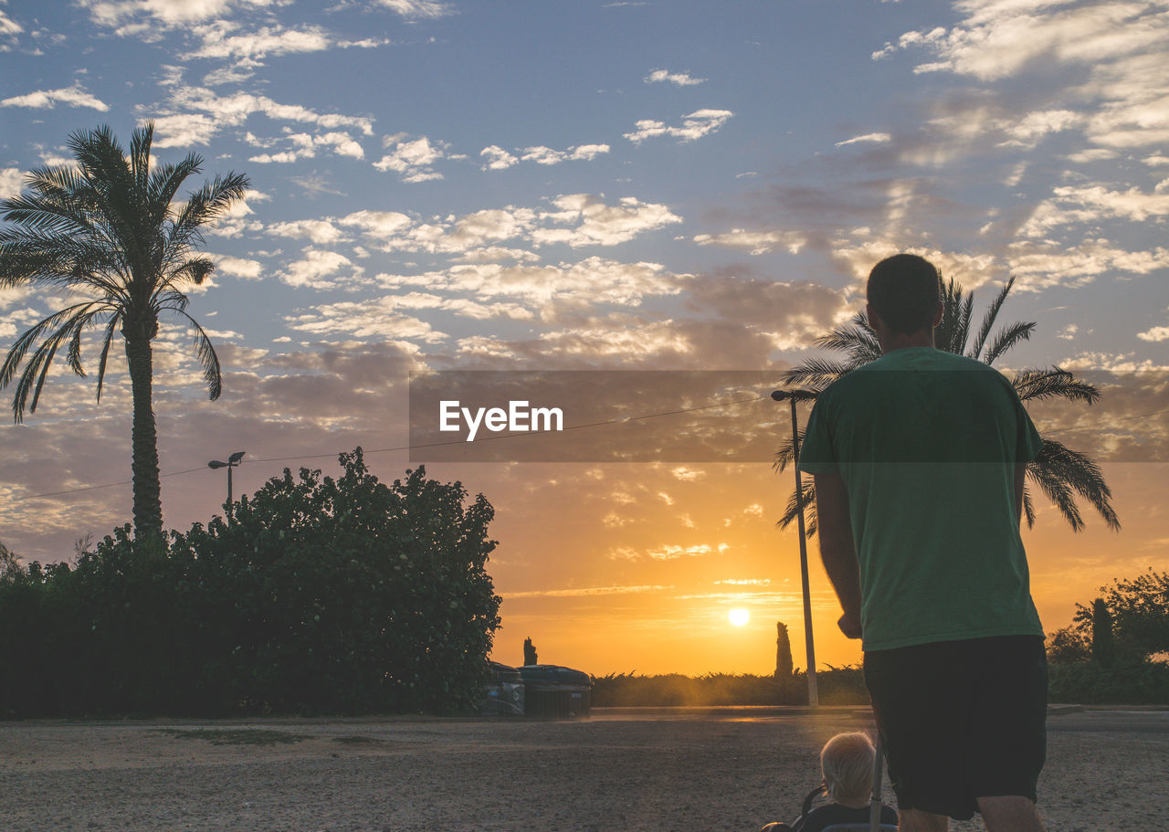 Rear view of father pushing baby in toy during sunset