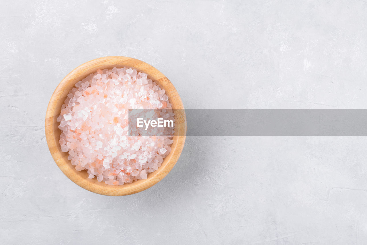 Pink himalayan salt in a wooden bowl on a light grey background, top view, flat lay, view from above