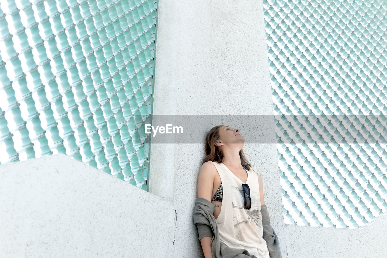 YOUNG WOMAN LOOKING AWAY AGAINST WALL