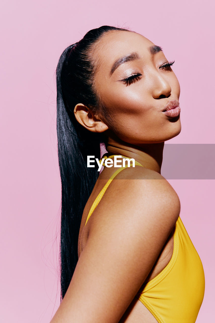 close-up portrait of young woman against pink background