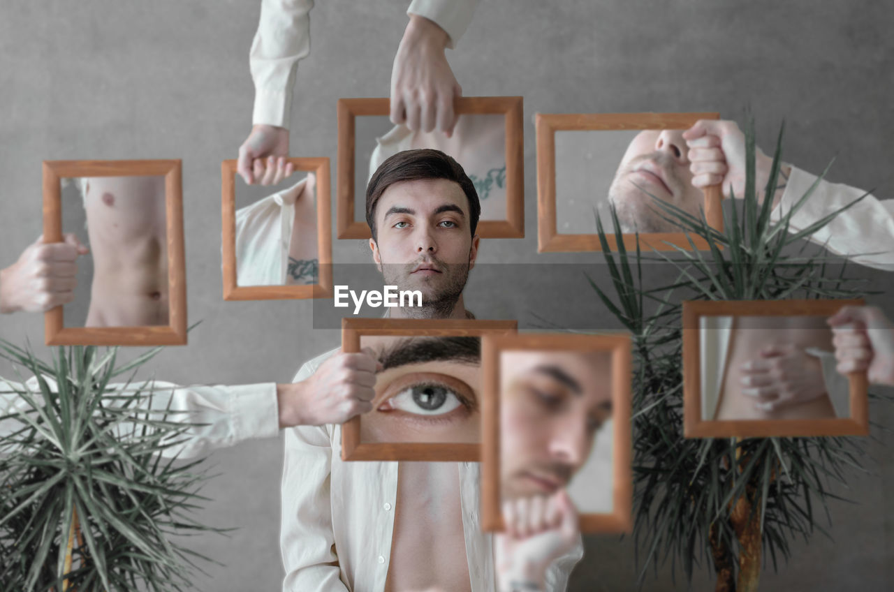 Digital composite image of hands holding picture frames around man standing against wall