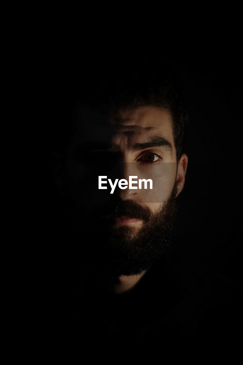 Close-up portrait of bearded man against black background