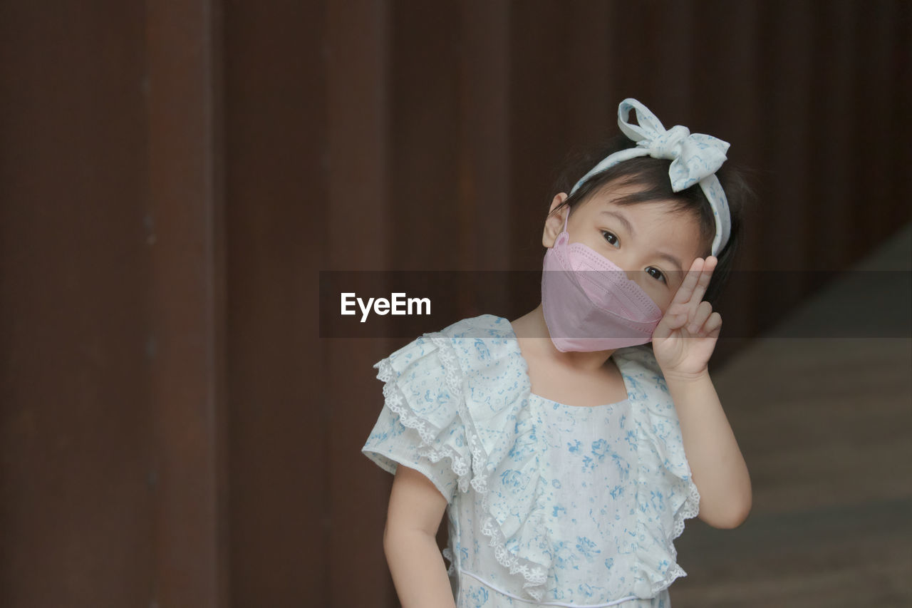 Happy charming 4 years old cute baby asian girl wear face mask raising her 2 fingers up.