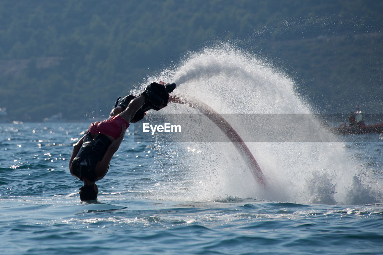 Man flyboarding in sea against mountains