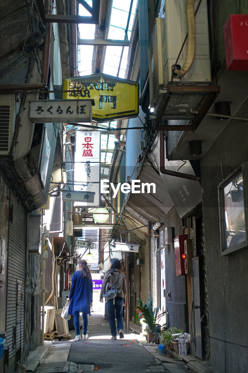 Rear view of women walking on street amidst buildings