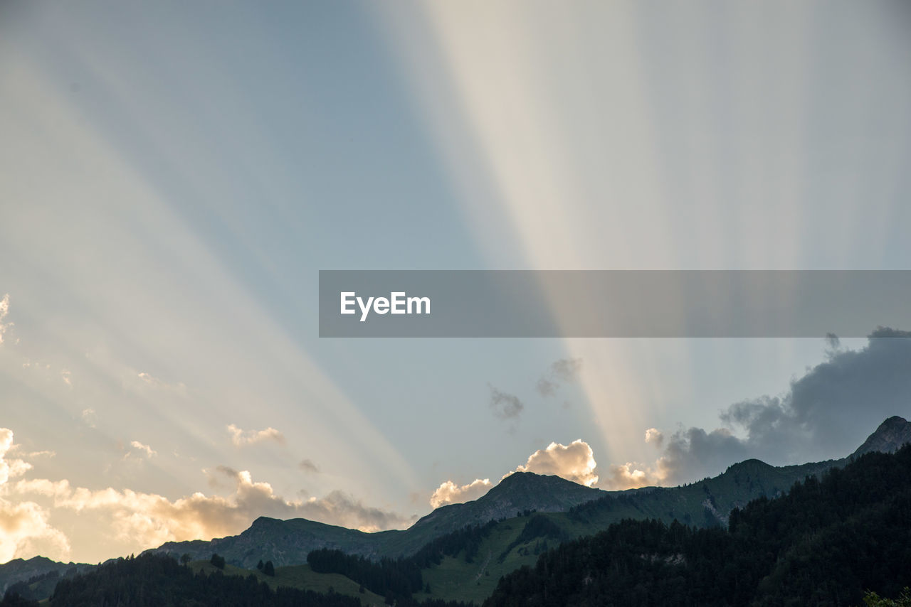 SUNLIGHT STREAMING THROUGH CLOUDS OVER MOUNTAIN