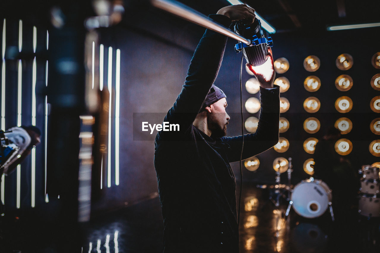 SIDE VIEW OF MAN WORKING AT ILLUMINATED KITCHEN